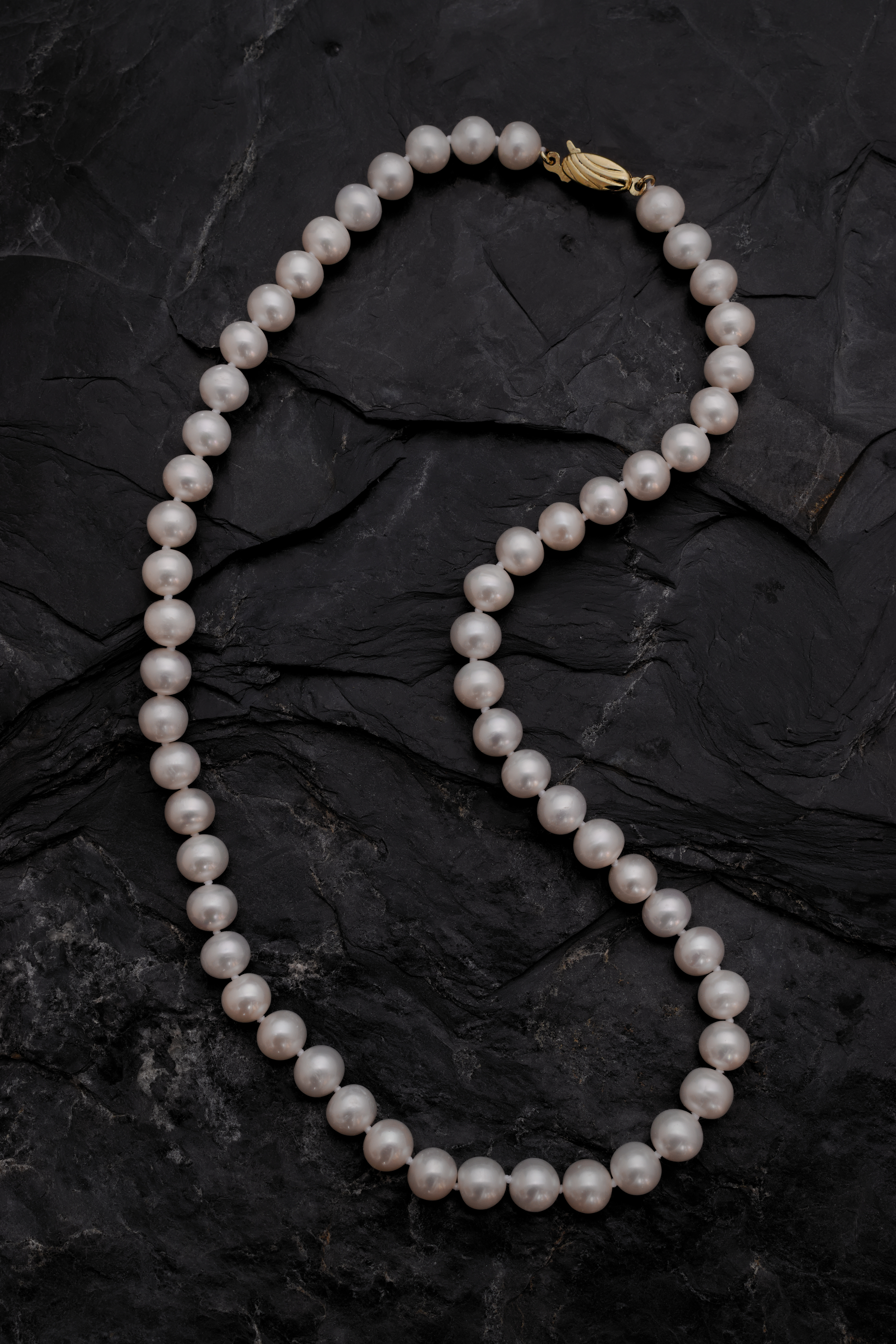 A white pearl necklace lying on a black slate background